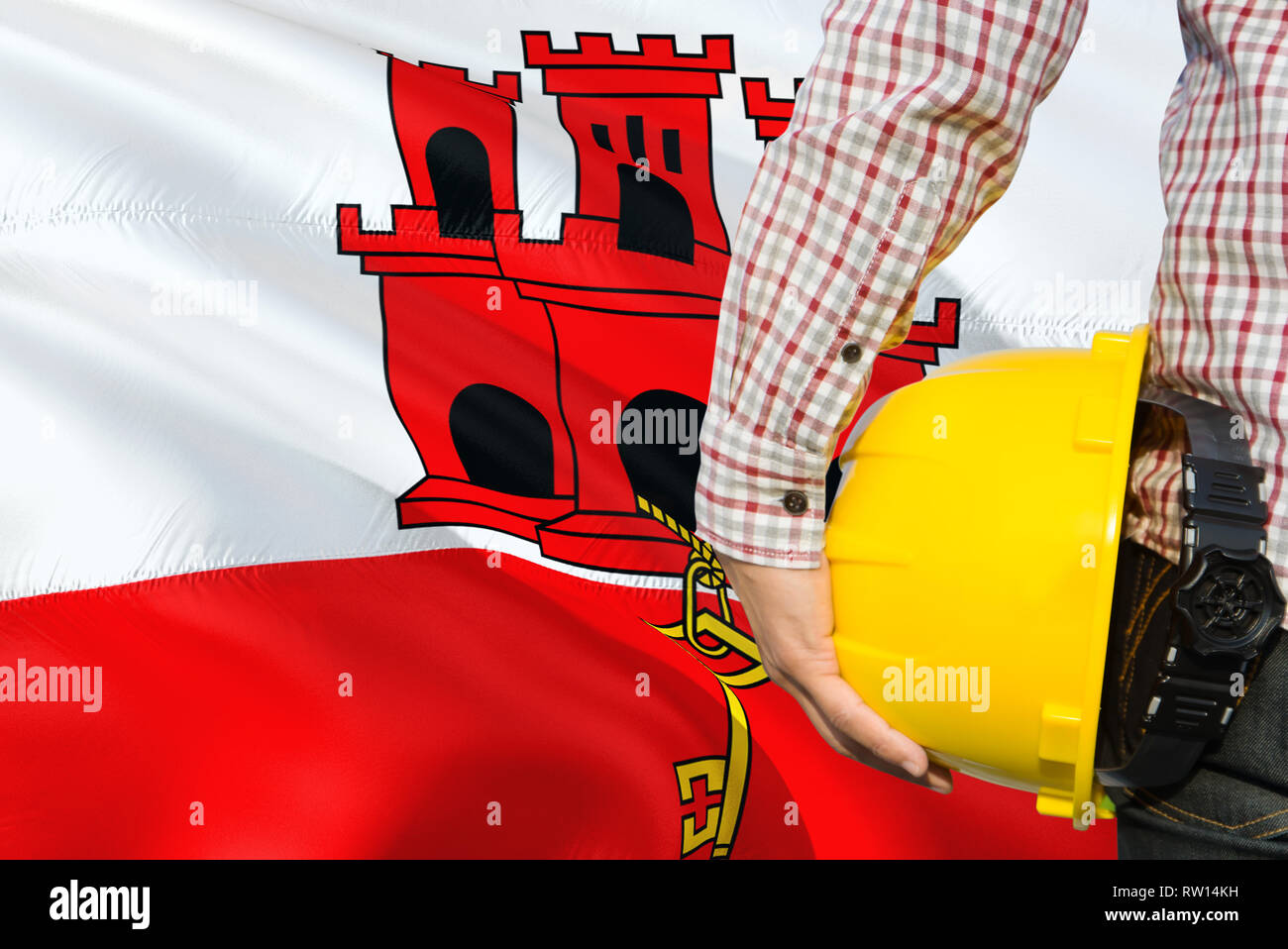 Engineer is holding yellow safety helmet with waving Gibraltar flag