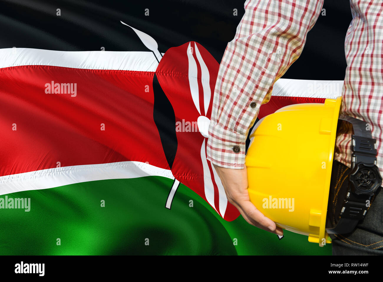 Kenyan Engineer is holding yellow safety helmet with waving Kenya flag background. Construction
