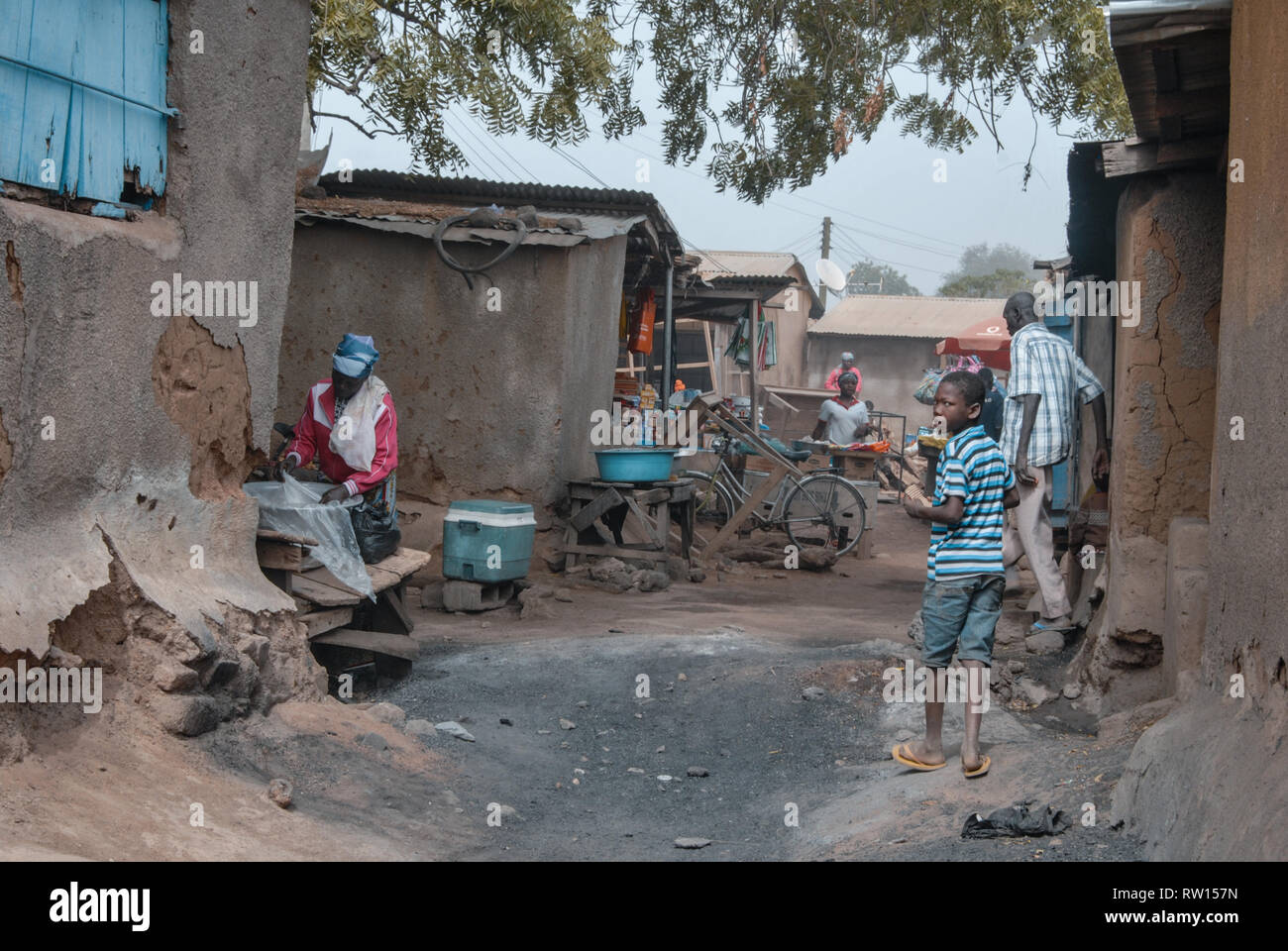 A photo of people walking and working in the dirty back alley of a street in Bolgatanga city Stock Photo