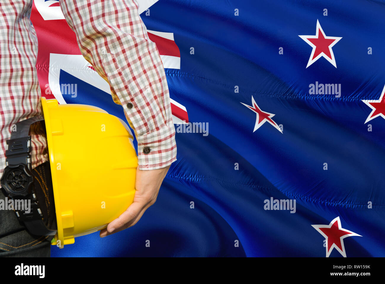 Engineer is holding yellow safety helmet with waving New Zealand flag