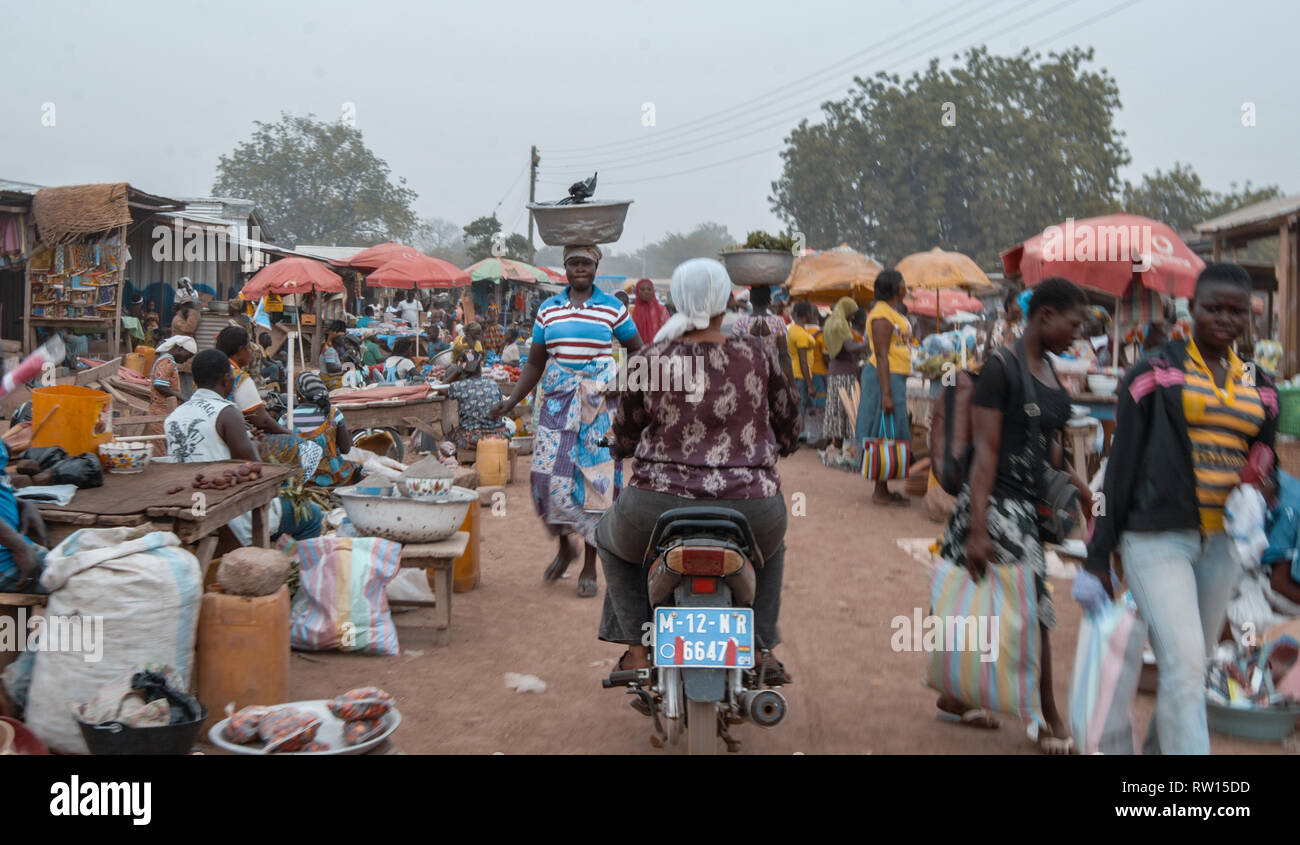 A photo of visitors and vendors passing by as they are visiting Bolgatanga (Bolga) farmer's market. Numerous stands can be seen at the street. Stock Photo