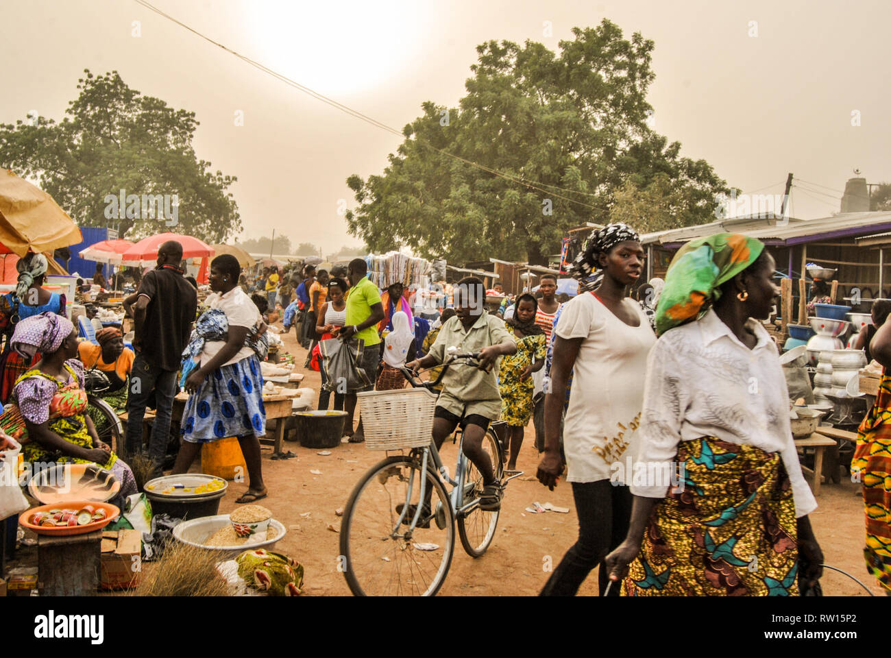 A nice photo of beautiful people visiting the fresh farmer's market in the town of Bolgatanga (Bolga), Ghana. A boy is riding a bicycle. Stock Photo