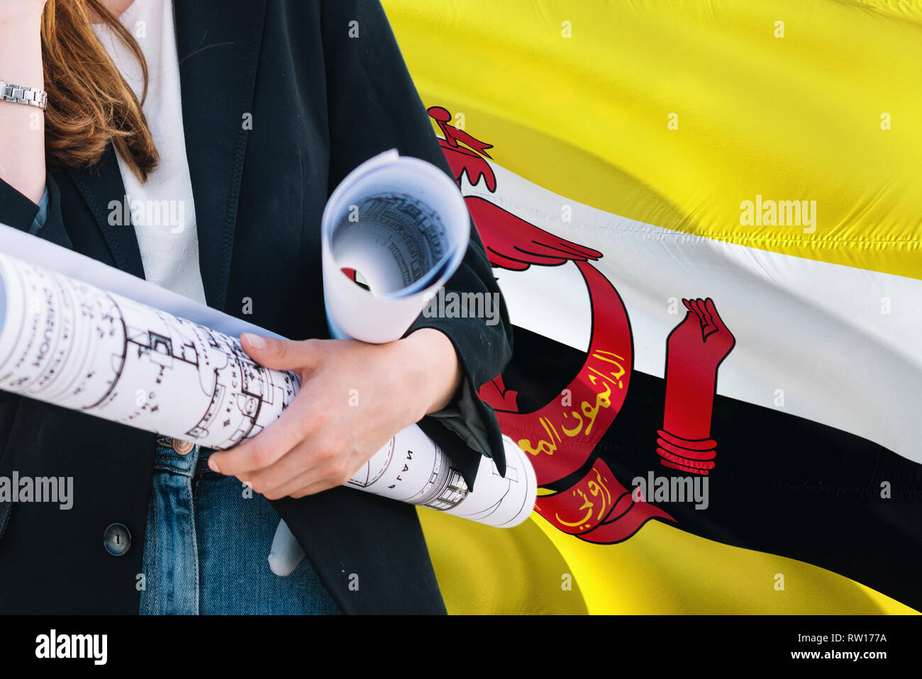 Bruneian Architect woman holding blueprint against Brunei waving flag background. Construction and architecture concept. Stock Photo