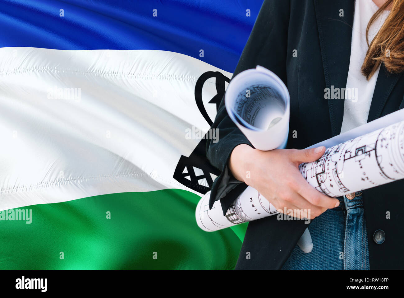 Architect woman holding blueprint against Lesotho waving flag background. Construction and architecture concept. Stock Photo