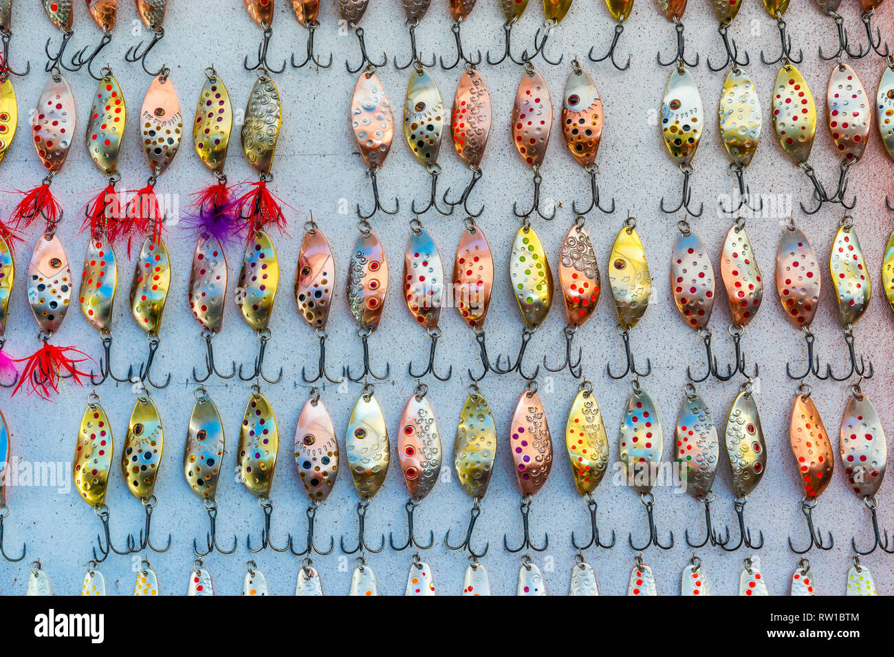 Countless of colorful fishing metal lures. Bait for fishing in the shape of a spoon with a hook on a gray background Stock Photo