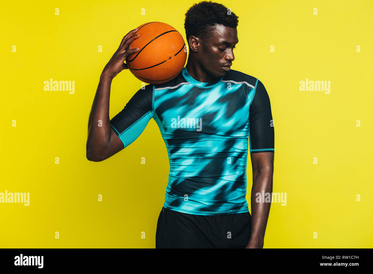 African man with basketball on his shoulder. Male basketball player against yellow background. Stock Photo