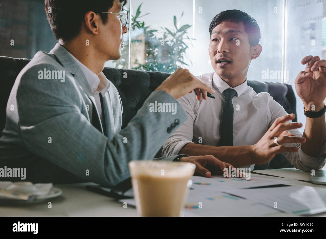 Two business people discussing new project in coffee shop. Young asian business professional explaining some points to his colleague sitting by, at ca Stock Photo