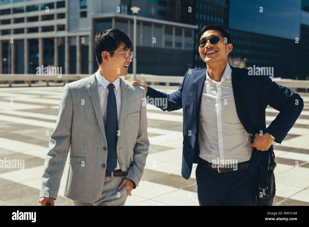 Two smiling asian businessmen talking and walking in the city. Business ...