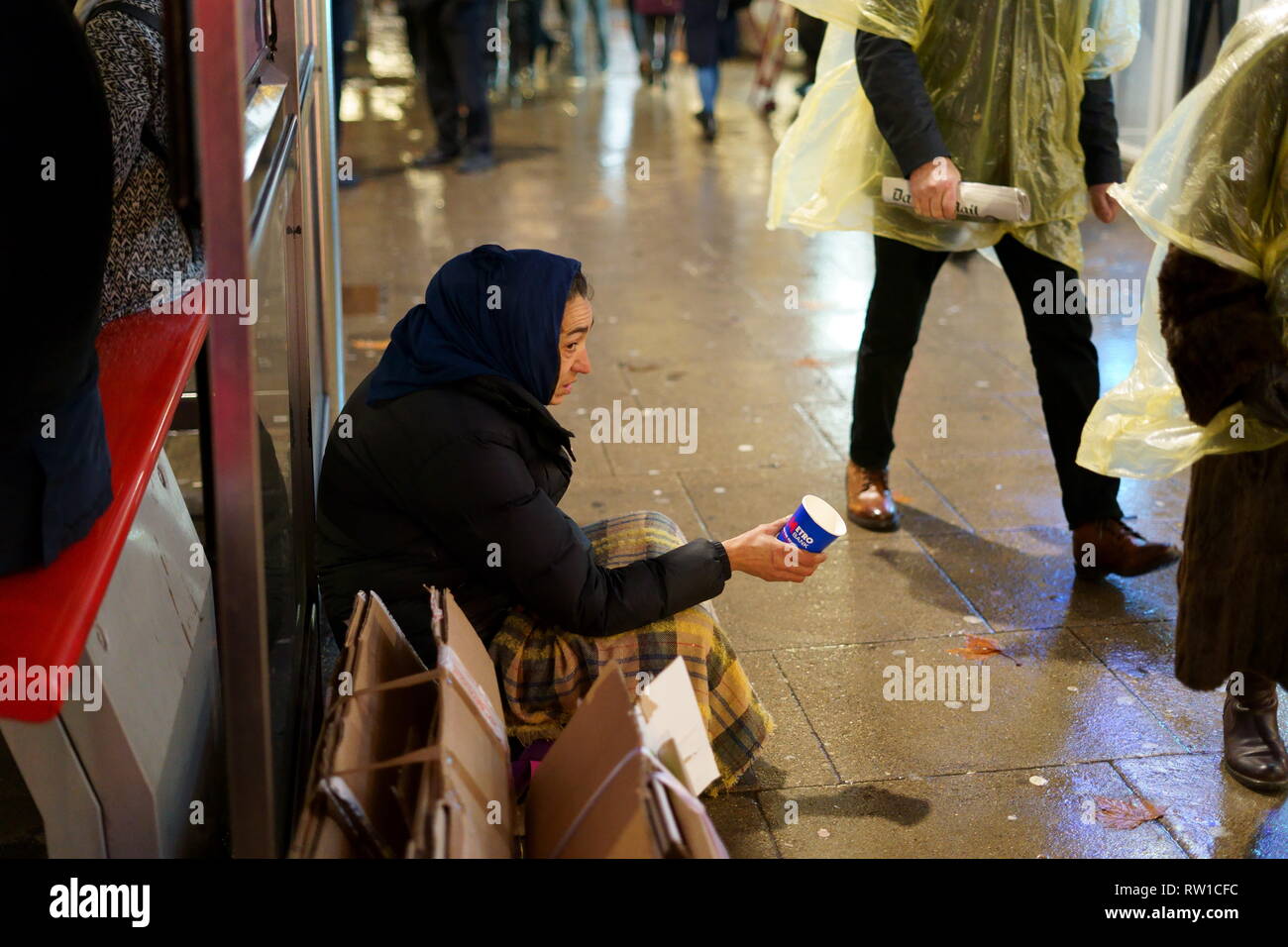 Homeless lady in London, sitting next to a bus stop as people walk passed her. Stock Photo