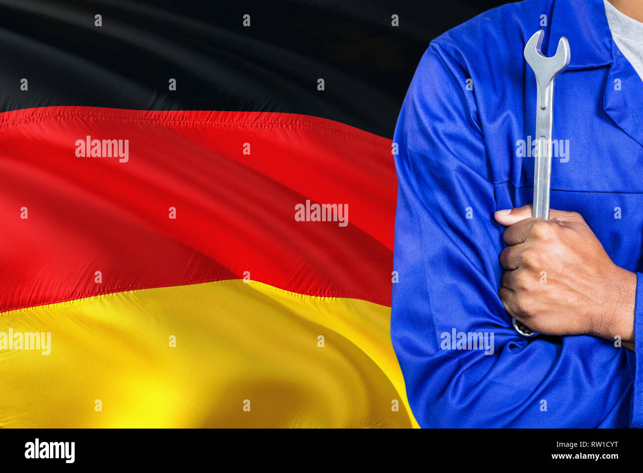 German Mechanic in blue uniform is holding wrench against waving