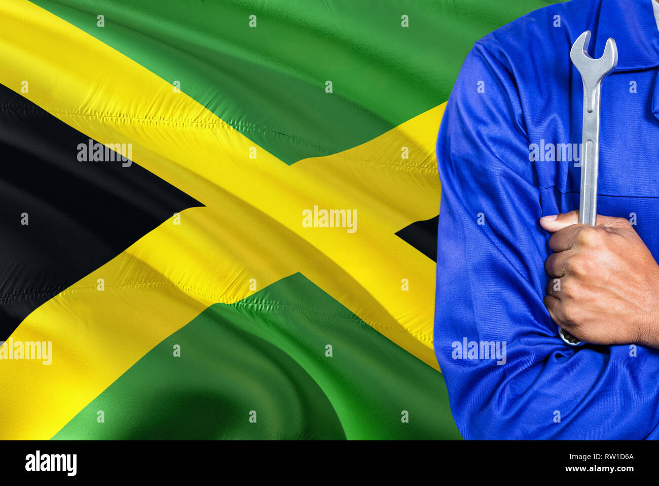 Jamaican Mechanic in blue uniform is holding wrench against waving