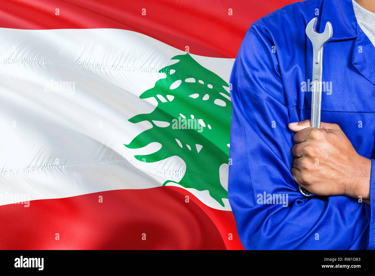 Lebanese Mechanic in blue uniform is holding wrench against waving Lebanon flag background