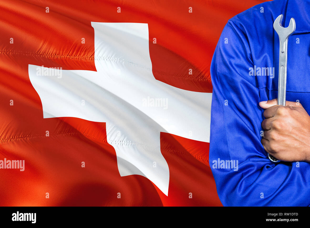 Swiss Mechanic in blue uniform is holding wrench against waving Switzerland  flag background. Crossed arms technician Stock Photo - Alamy