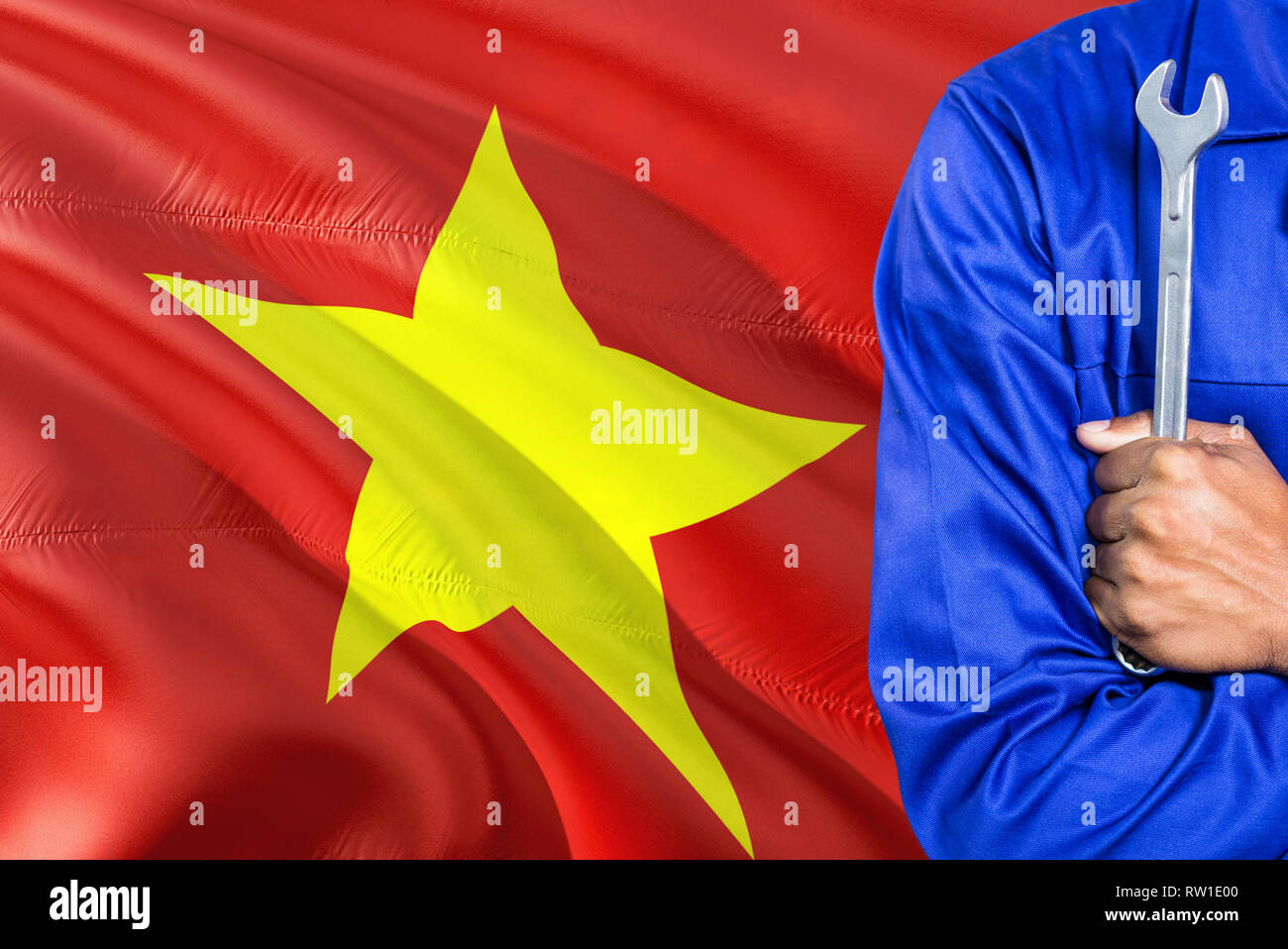 Vietnamese Mechanic in blue uniform is holding wrench against waving Vietnam flag background