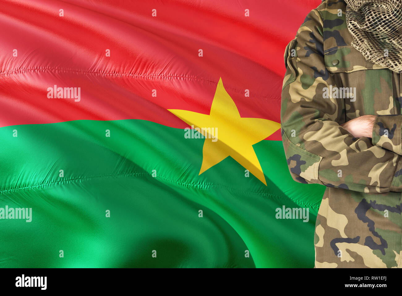 Crossed arms soldier with national waving flag on background - Burkina Faso Military theme. Stock Photo