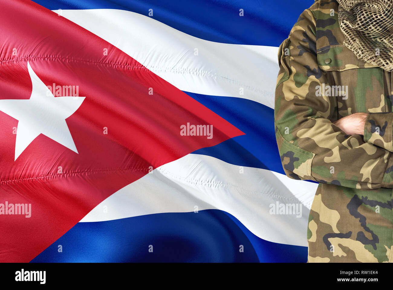 Crossed arms Cuban soldier with national waving flag on background - Cuba Military theme. Stock Photo