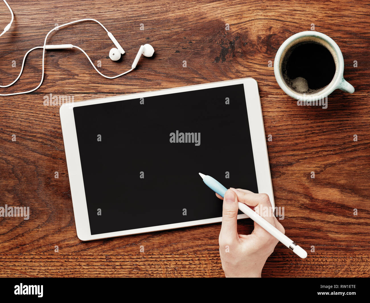 Digital tablet and cup of coffee on a wooden table. A pencil in hand. Calligraphy and lettering mockup. Flat lay. Stock Photo