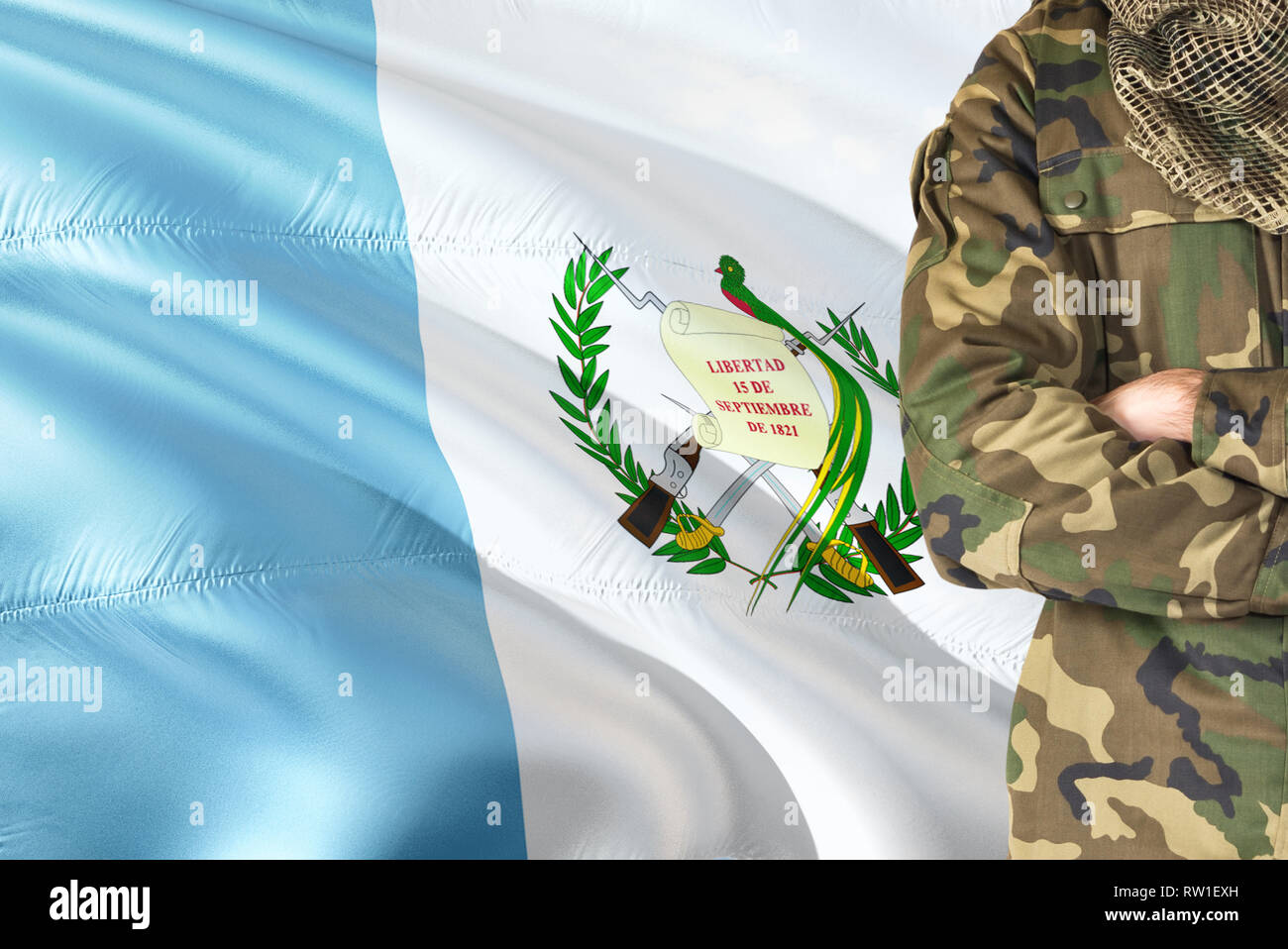 Crossed arms Guatemalan soldier with national waving flag on background - Guatemala Military theme. Stock Photo
