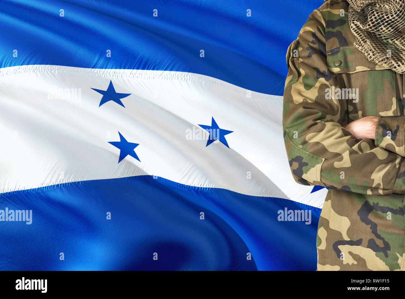 Crossed arms Honduran soldier with national waving flag on background - Honduras Military theme. Stock Photo