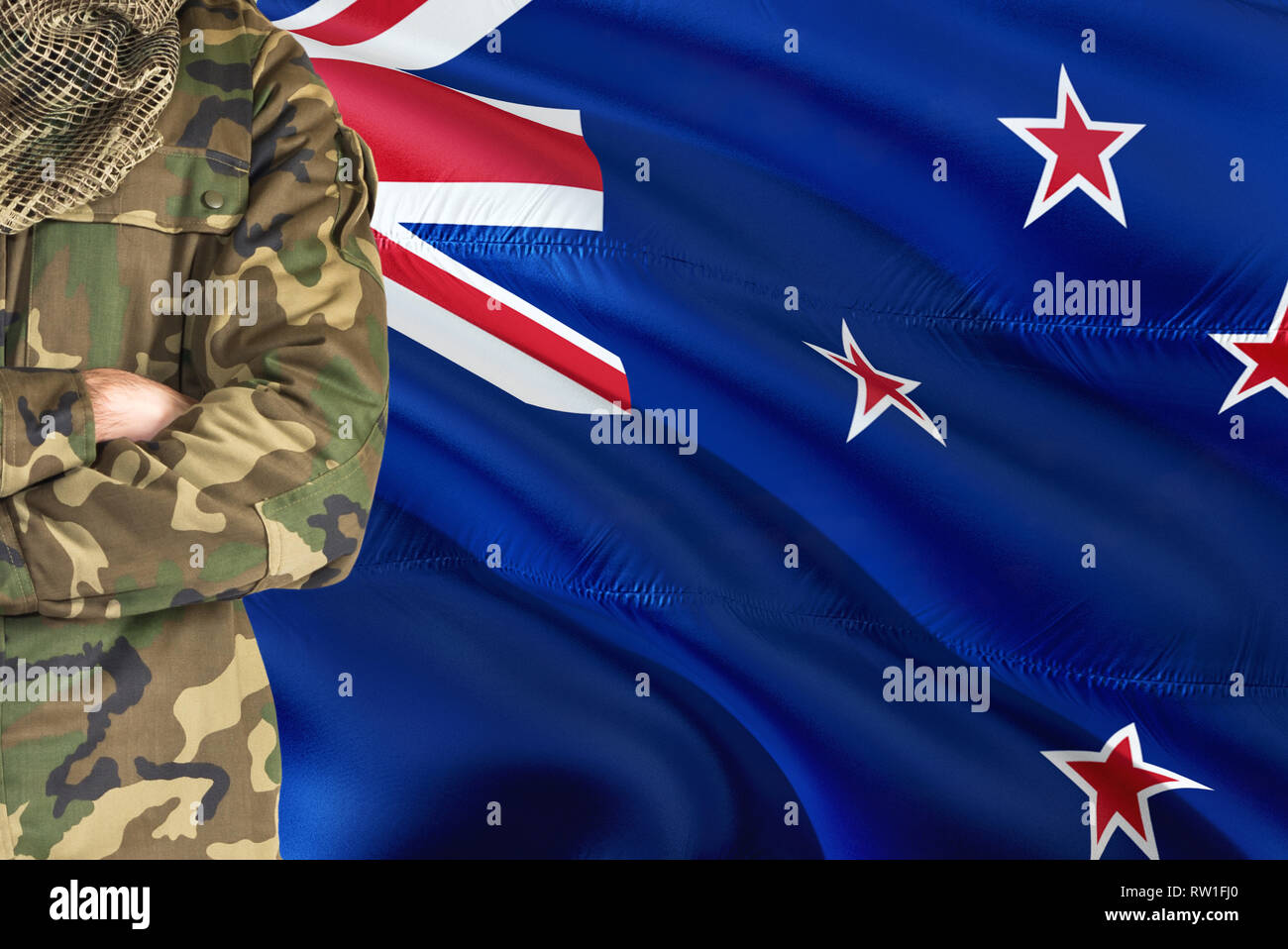 Crossed arms soldier with national waving flag on background - New Zealand Military theme. Stock Photo