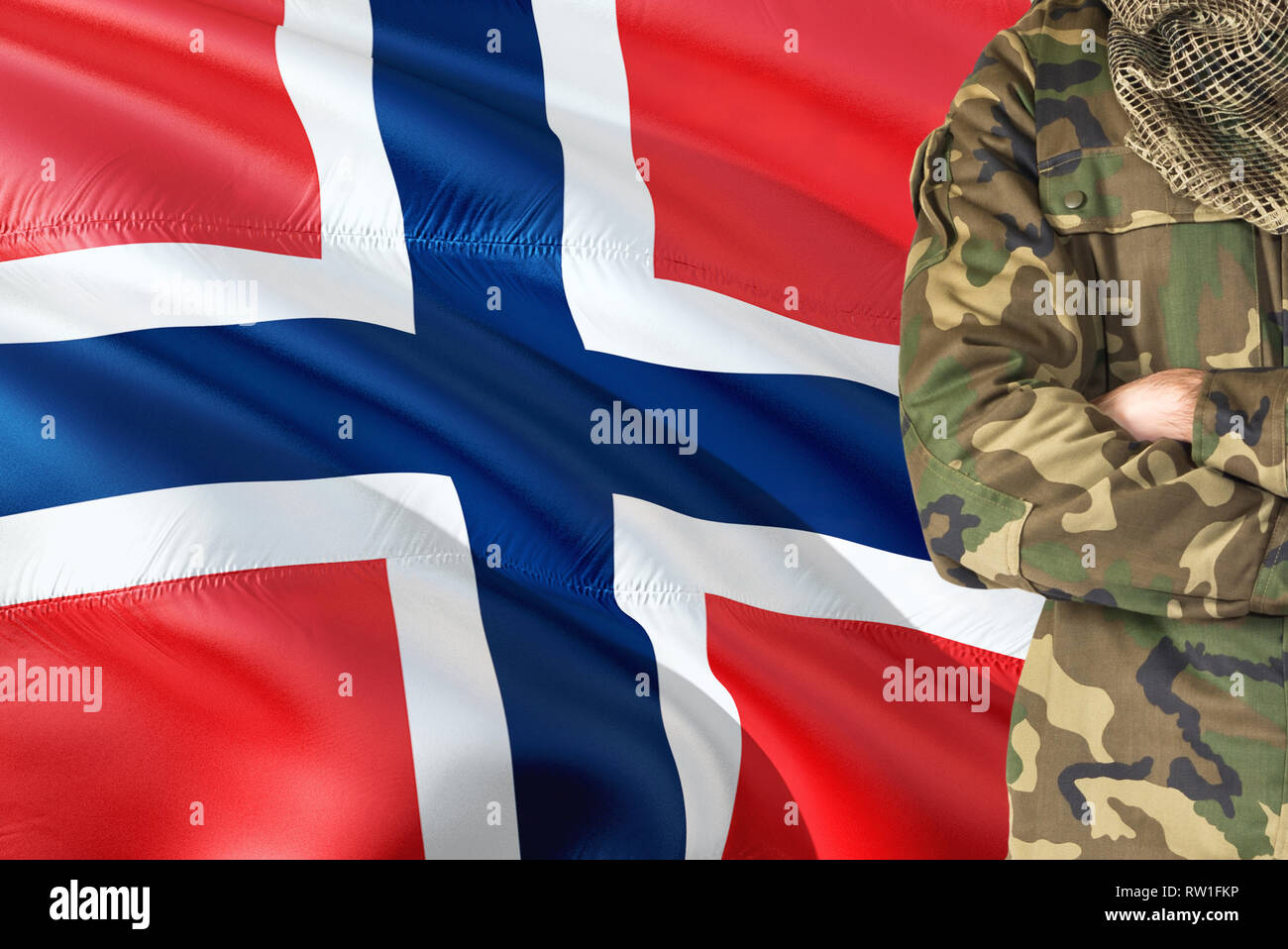 Crossed arms Norwegian soldier with national waving flag on background - Norway Military theme. Stock Photo