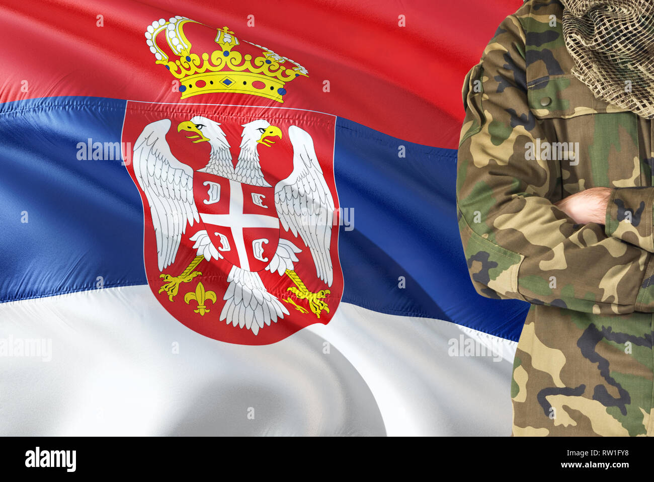Crossed arms Serbian soldier with national waving flag on background - Serbia Military theme. Stock Photo