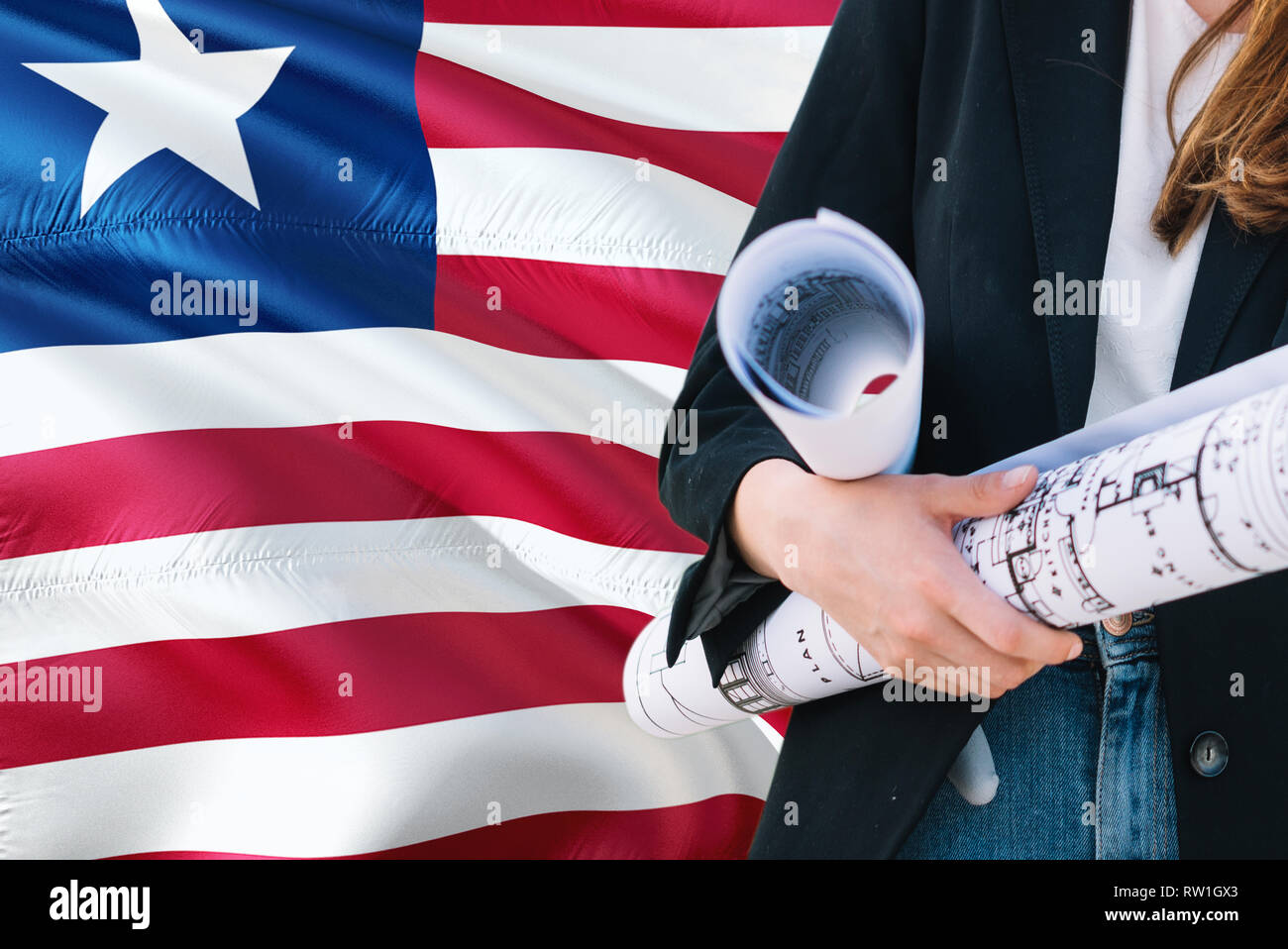 Liberian Architect woman holding blueprint against Liberia waving flag background. Construction and architecture concept. Stock Photo