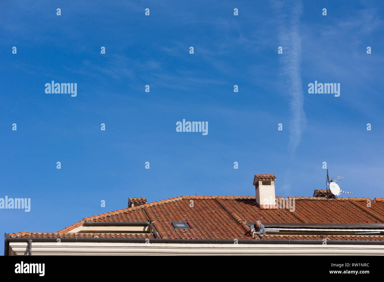 Man leaning from a roof terrace masticing, silicon sealant, fixing, sealing, terracota roof tiles in Spain. Stock Photo