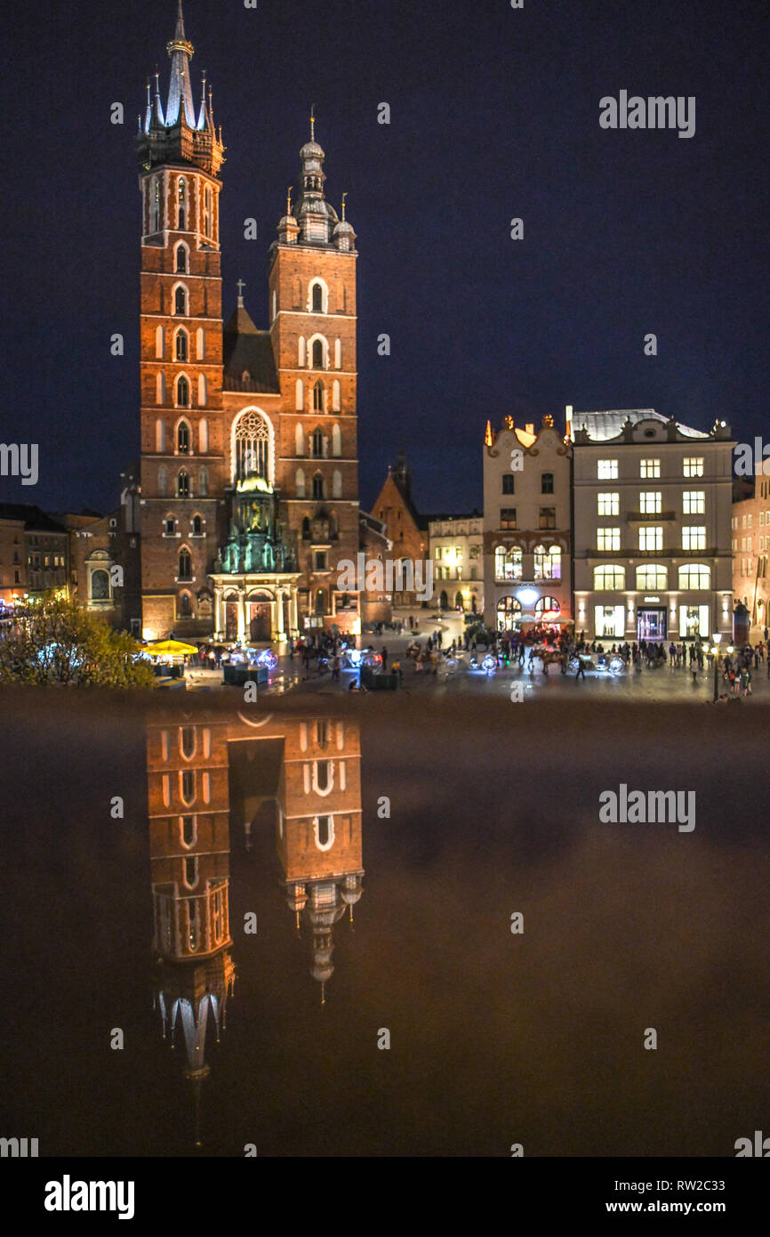 Exterior of Church of Our Lady Assumed into Heaven (St. Mary's Basilica) reflects on shiny surface at night in the Main Market Square of Krak—w Old To Stock Photo