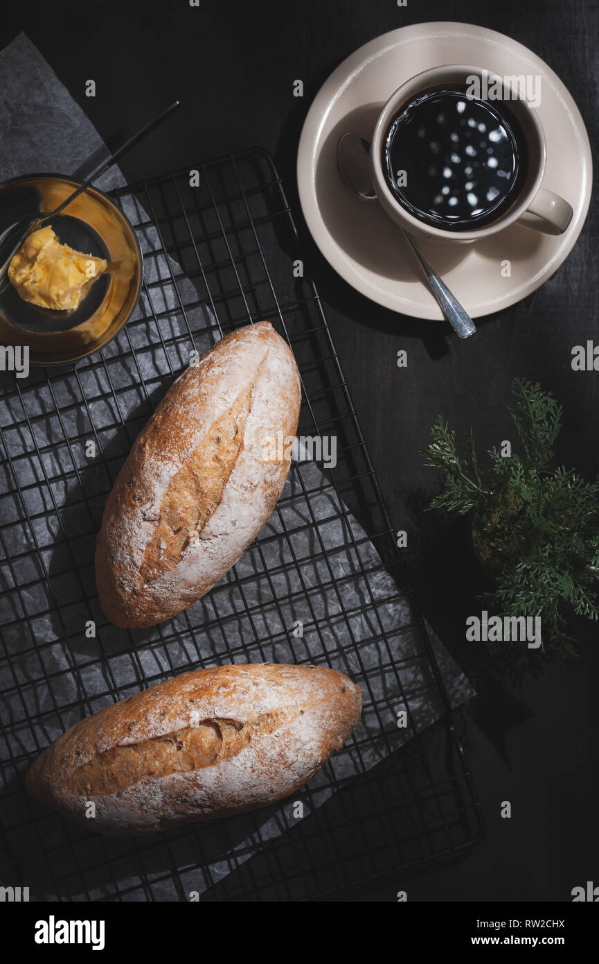 Top view of baguette, European style bread with margarine and black coffee on black wood table in early morning time with hard light effect. Organic a Stock Photo