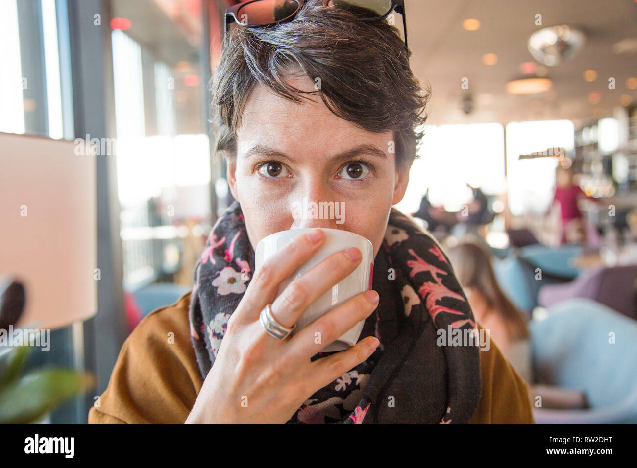 Portrait of a beautiful young woman in warm clothes sitting in cafe and drinkg coffee, blurred background, head and shoulders Stock Photo