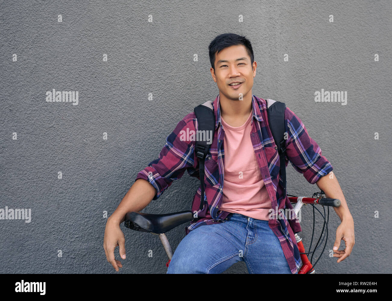 Smiling young man leaning with his bike against a wall Stock Photo