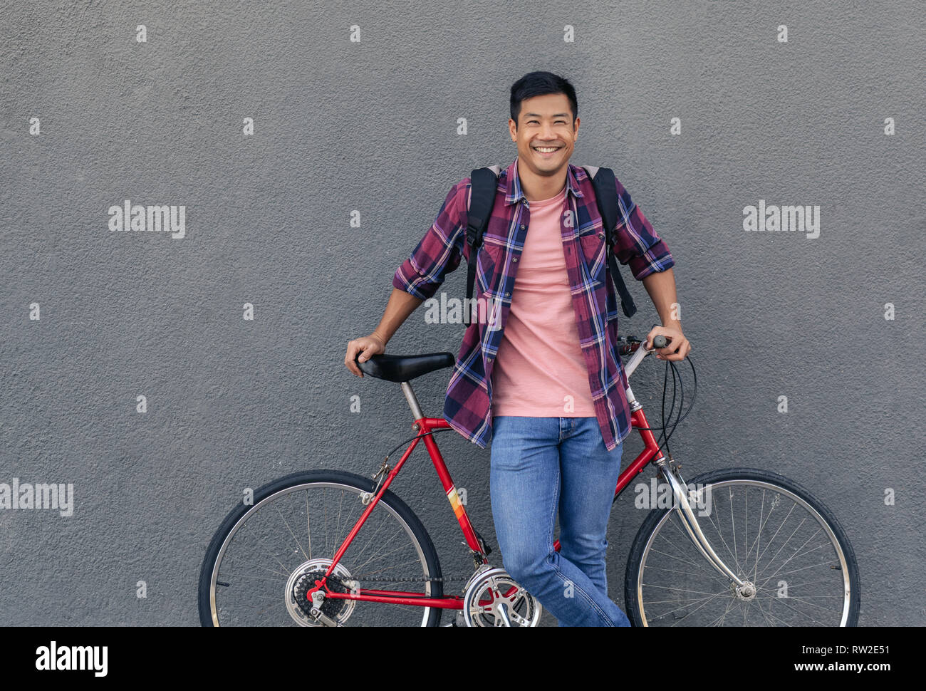 Cool smiling man standing with his bike against a wall Stock Photo