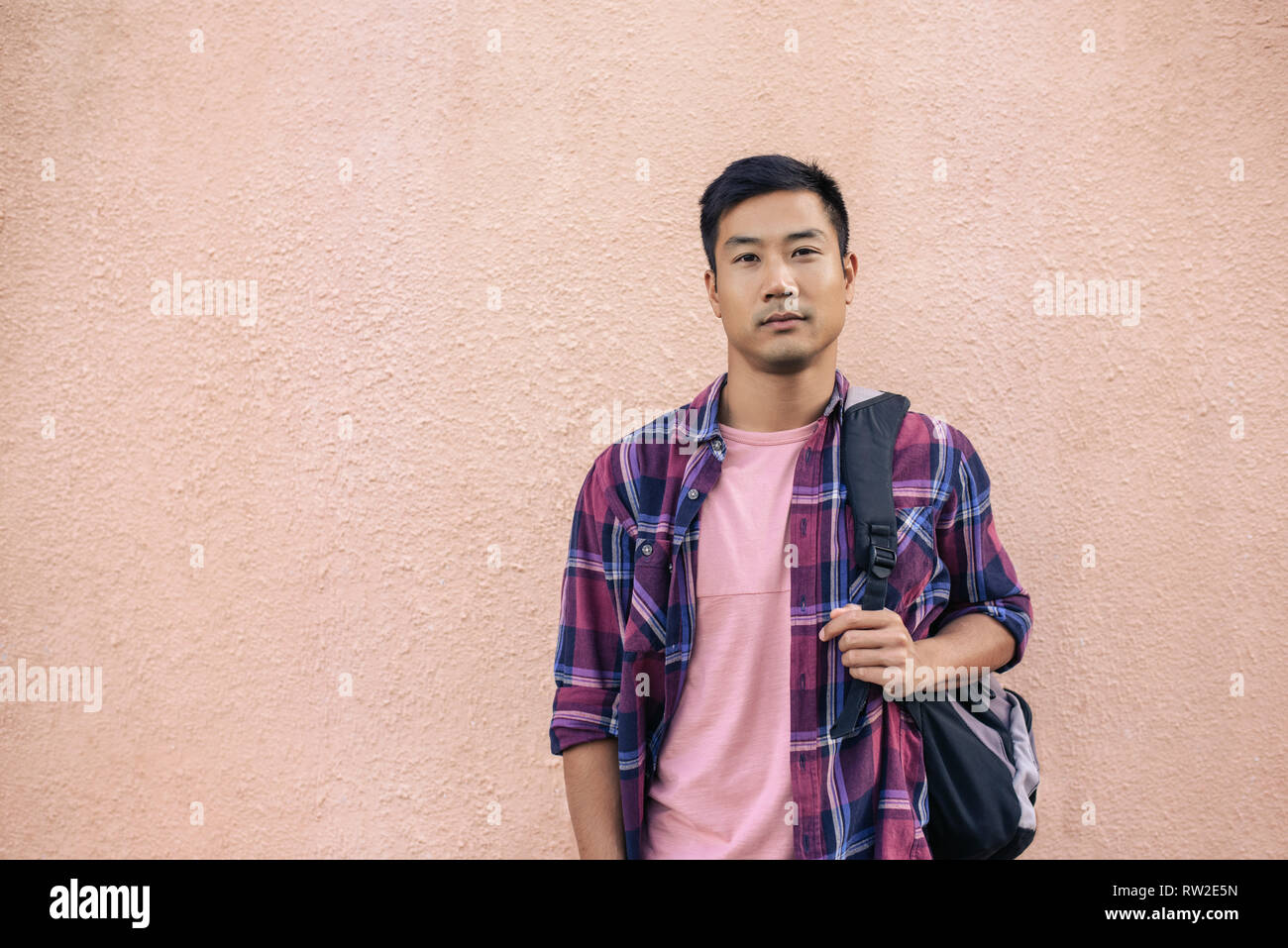 Confident young Asian man standing outside carrying a backpack Stock Photo