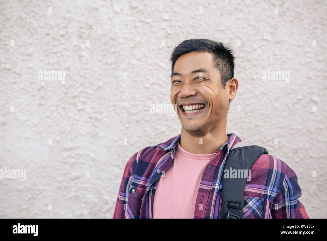 Young Asian man standing on a city street laughing Stock Photo