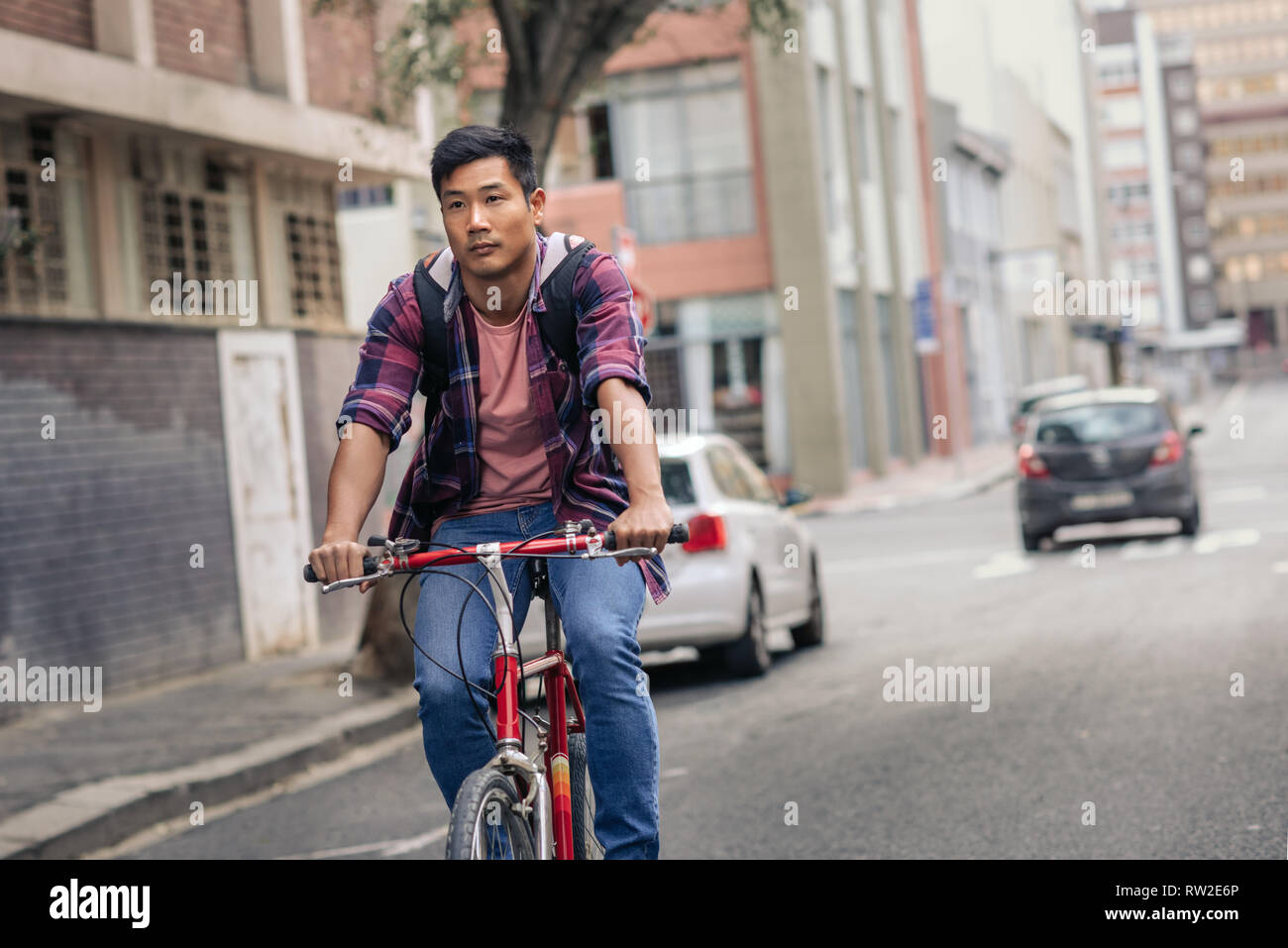 Young Asian man riding his bike through city streets Stock Photo