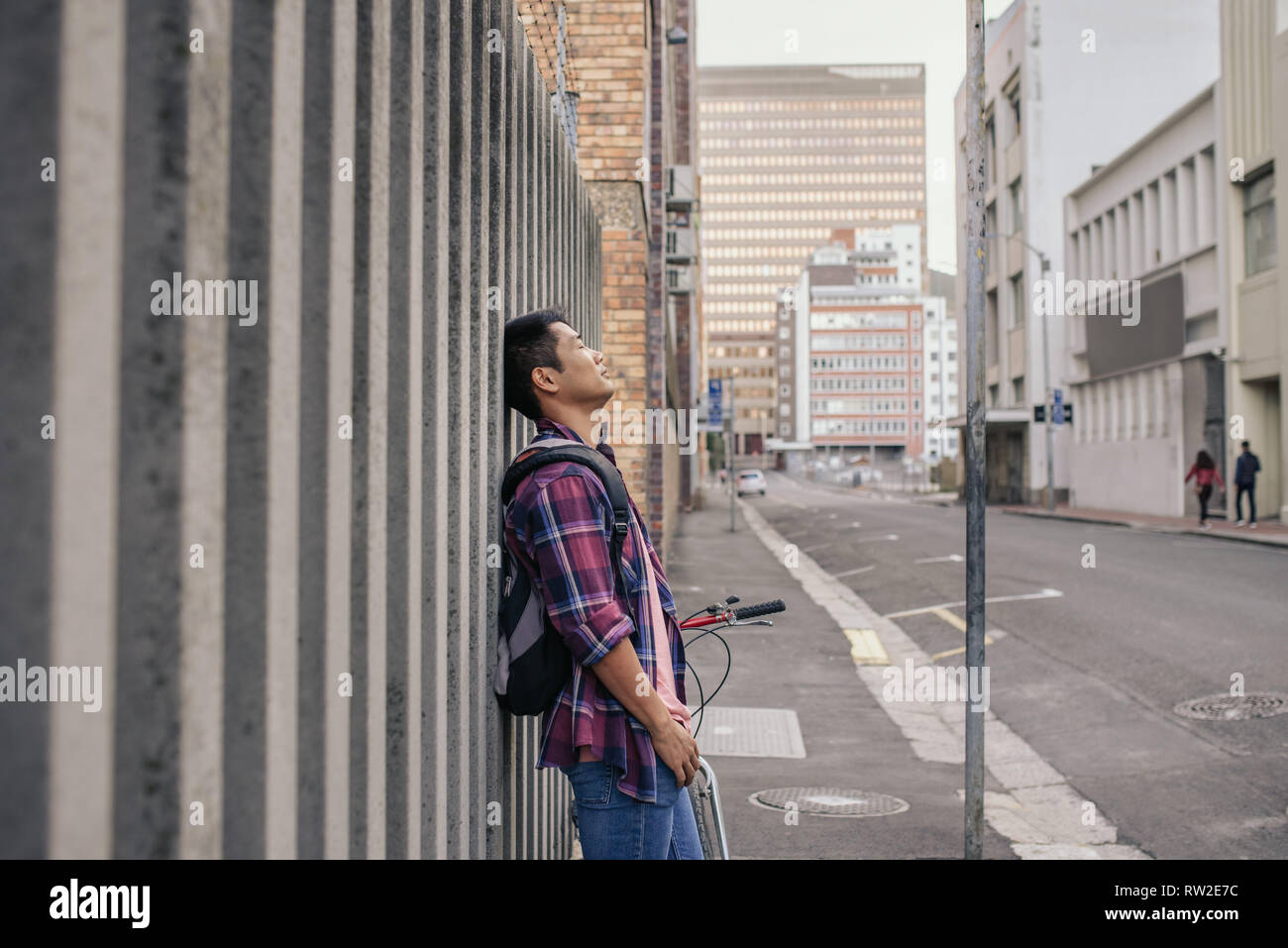 Young man with eyes closed leaning against a city wall Stock Photo