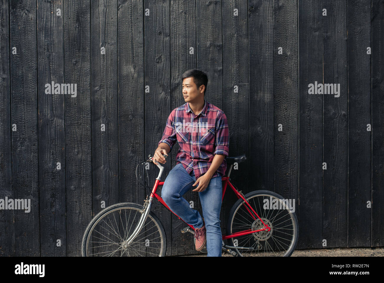 Young man with a bike leaning against a city wall Stock Photo