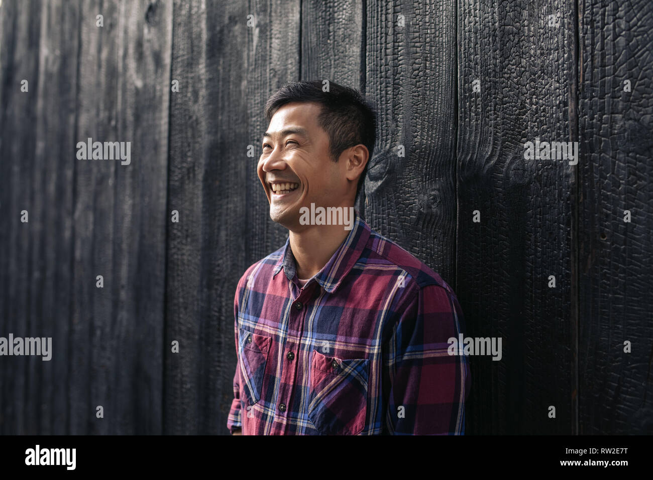 Laughing Asian man leaning against a wall in the city Stock Photo