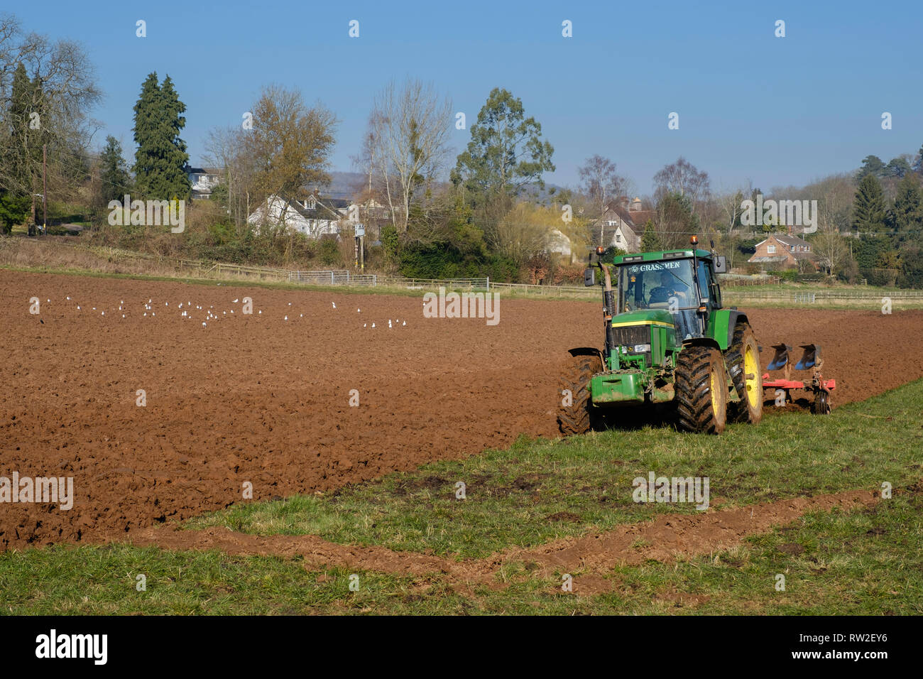 SPRING PLOUGHING WITH GREEN TRACTOR IN FIELD IN GLOUCESTERSHIRE ENGLAND UK Stock Photo