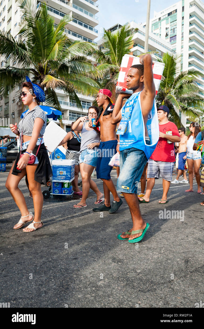RIO DE JANEIRO - JANUARY 30, 2016: A young Brazilian vendor carries a drink cooler through a Carnival street party in Ipanema. Stock Photo