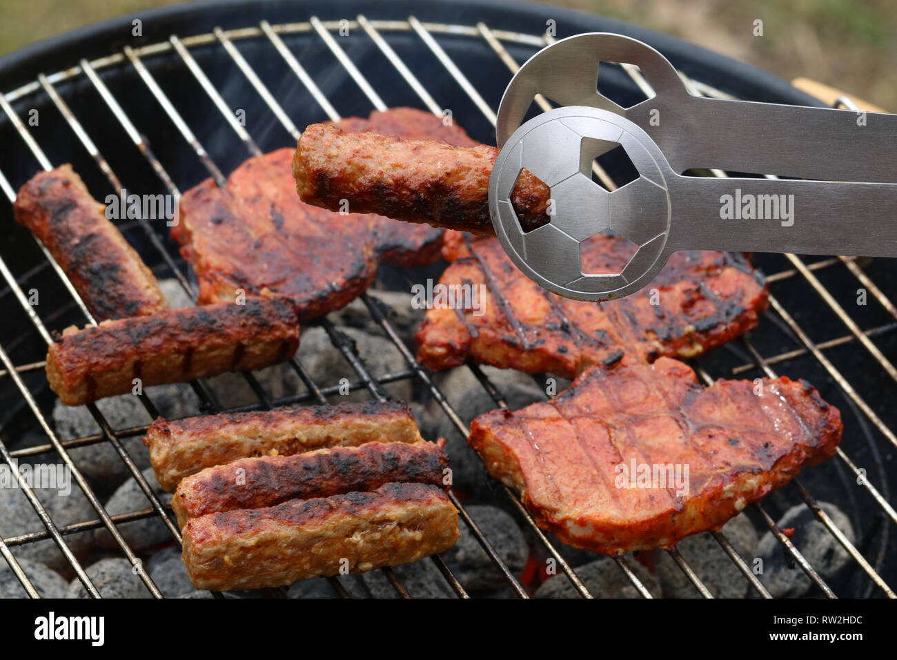 close up of tasty steaks and cevapcici on barbecue grill with Football World Cup tong Stock Photo