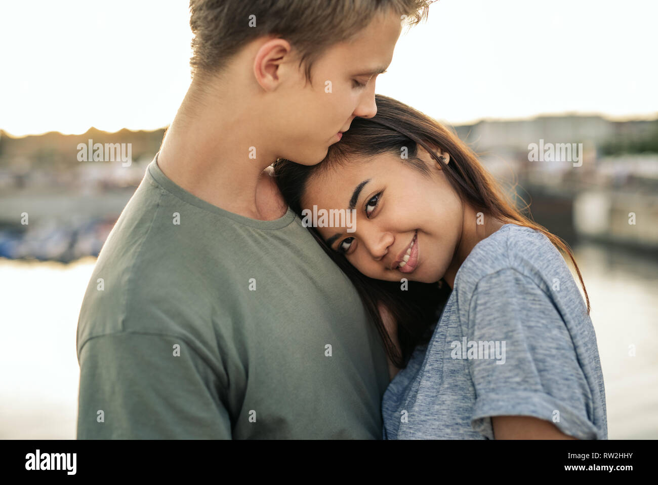 Smiling young woman hugging her boyfriend outside by a harbor Stock Photo