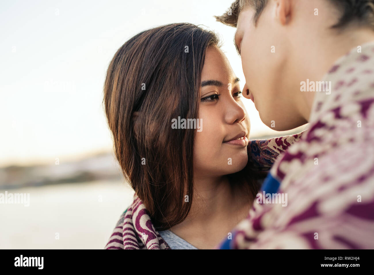 Young couple wrapped in a blanket about to kiss outside Stock Photo