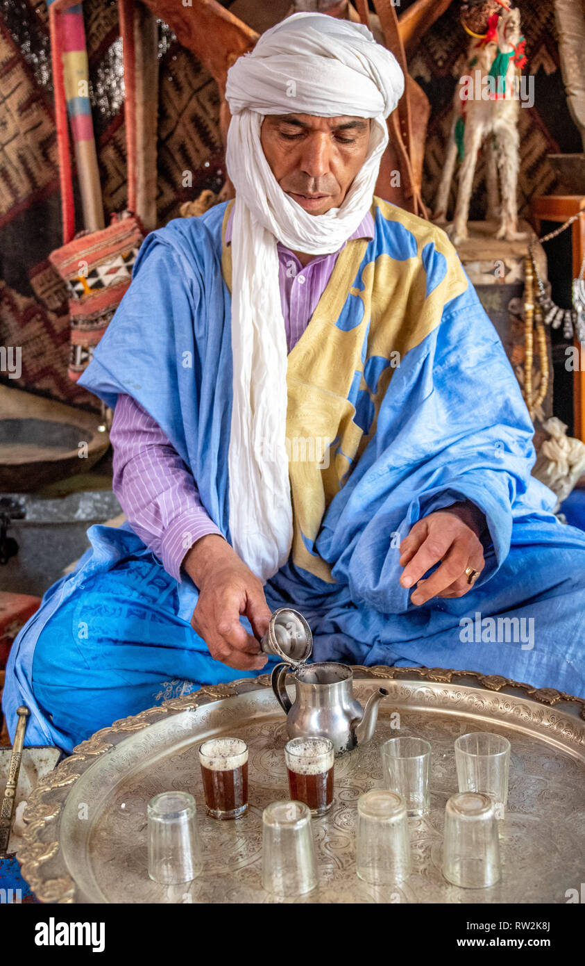 Berber man wearing turban and deraa opens up lid of teapot for