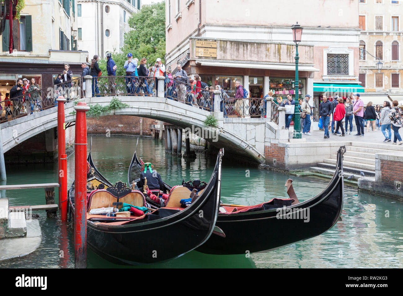 Two moored gondolas on a back canal at Campo dei Santi Apostoli, Cannaregio, Venice, Veneto, Italy with tourists on a bridge crossing the canal. Low a Stock Photo
