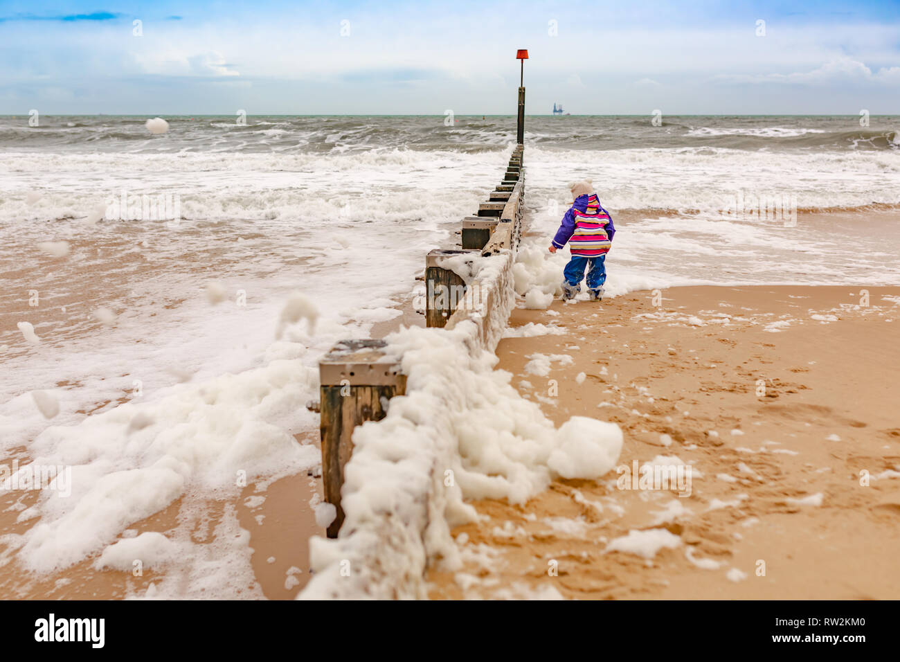 Landscape photograph taken on beach of sea with young child with back to camera playing in sea foam. Bournemouth, Dorset, UK. Stock Photo
