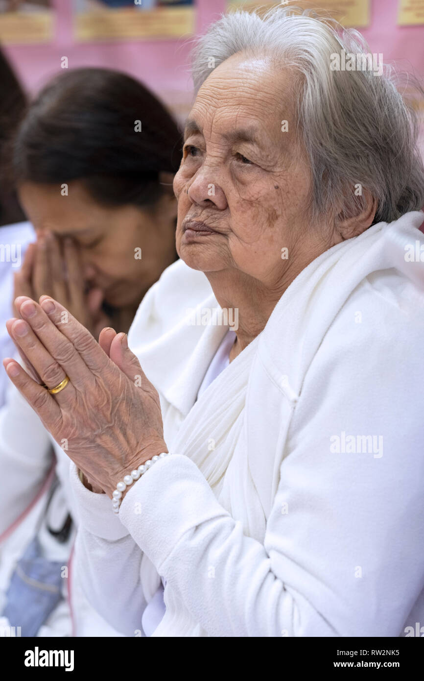 Devout Buddhist women in white praying & meditating at a service at a temple in Elmhurst, Queens, New York City. Stock Photo