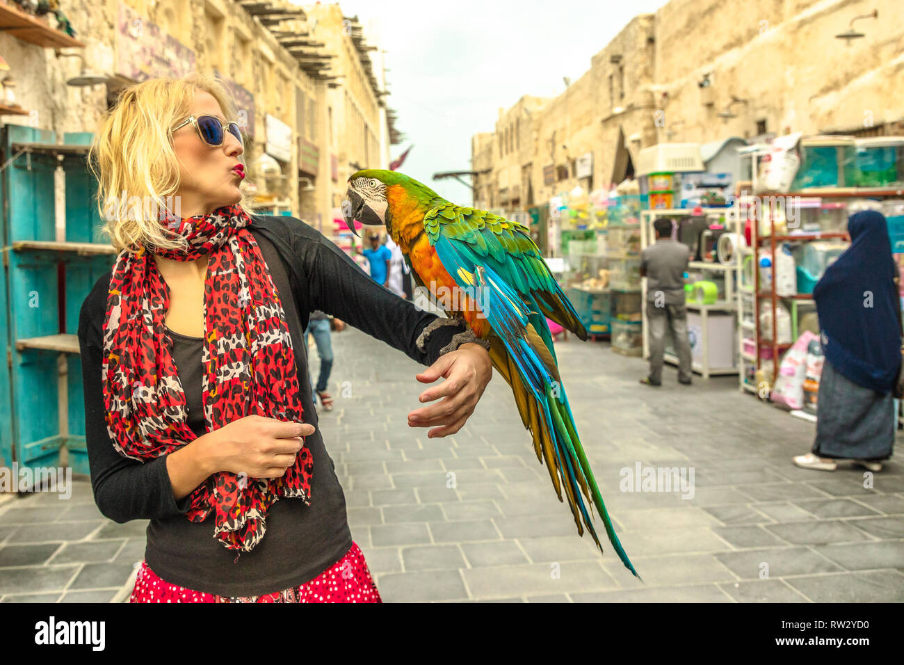 Happy woman kisses a parrot at Bird Souq inside Souq Waqif, the old market and tourist attraction in Al Souq District, Doha city center, Qatar Stock Photo