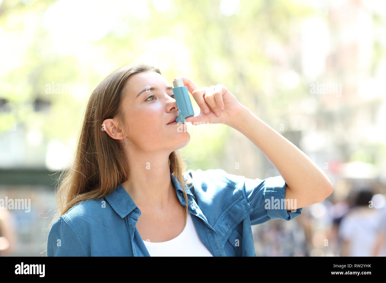 Asthmatic woman having an attack using asthma inhaler standing in the street Stock Photo